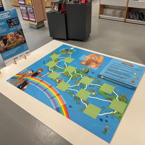 Foto af spillepladen på gulvet, en infotavle og en gul skumterning.